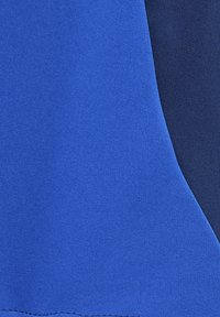 Blauwe stof met een gladde textuur, met een color-block ontwerp. Een donkerdere blauwe sectie is aangrenzend, wat een contrasterend effect creëert.