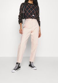 Jeans de tiro alto en rosa claro combinados con un suéter oscuro de estampado y zapatillas negras de caña alta. Tejido texturizado con un corte relajado.