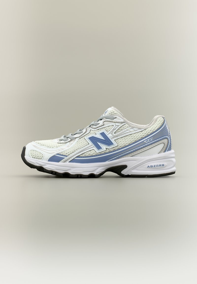 Λευκό και ανοιχτό μπλε αθλητικό παπούτσι New Balance 740 με γκρι κορδόνια και μαύρη σόλα σε απλό μπεζ φόντο.