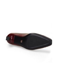 Chaussure en cuir verni rouge avec un bout pointu, détail clouté le long du bord, et une semelle en caoutchouc noir texturé. Dispose d'une languette à l'arrière pour un enfilage facile.