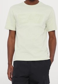 Světle zelené tričko s krátkým rukávem vyrobené z měkké tkaniny, s embosovaným logem "EA7" na hrudi a kulatým výstřihem.
