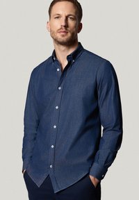 Granatowa koszula zapinana na guziki z denimu, z klasycznym kołnierzykiem, długimi rękawami oraz białymi guzikami na przodzie i mankietach.