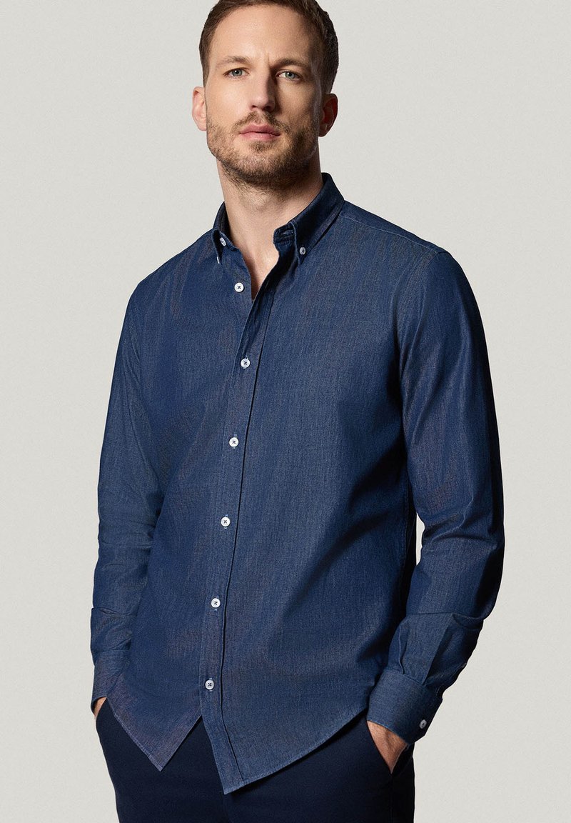 Granatowa koszula zapinana na guziki z denimu, z klasycznym kołnierzykiem, długimi rękawami oraz białymi guzikami na przodzie i mankietach.