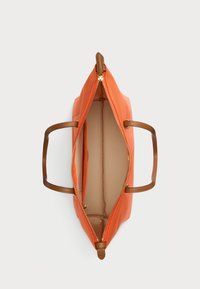 Πορτοκαλί τσάντα tote με καφέ δερμάτινες λαβές. Ο εσωτερικός χώρος διαθέτει μπεζ επένδυση και μια θήκη με φερμουάρ. Η λεπτομέρεια του φερμουάρ είναι σε χρυσό τόνο.