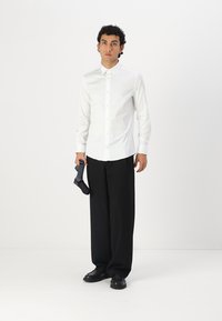 Camisa blanca de botones con un corte entallado, que presenta una textura suave. Combinada con pantalones negros de corte holgado y zapatos negros.
