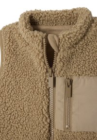 Beige Fleece-Weste mit hohem Kragen, strukturiertem Stoff, frontalem Reißverschluss und einer Klapptasche aus glattem Material auf der linken Seite.