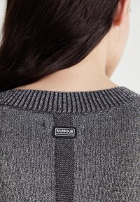 Pull en maille gris avec un col côtelé. Présente un motif texturé et une étiquette noire indiquant "BARBOUR INTERNATIONAL" au dos.