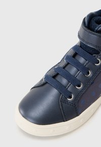 Marineblå lærersneaker med mesh-detaljer, gummisåle, rund tå og flate lisser. Har små blå prikker på siden.