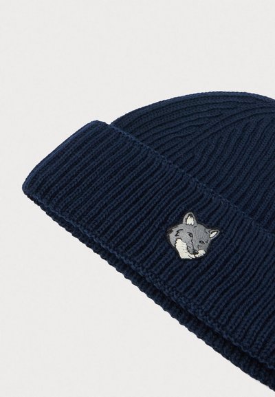 Căciulă din tricot ribbed de culoare bleumarin, cu bordură pliată și un mic cap de vulpe gri brodat în partea din față a bordurii.