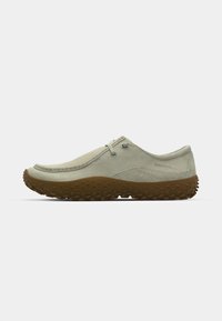 Zapatos slip-on de color verde claro con una suela de goma texturizada, diseñados para la comodidad, con una costura cosida y ojales de metal para los cordones.