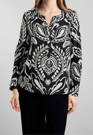Czarna bluzka w białe kwiatowe i paisley wzory, z zapięciem na guziki, długimi rękawami i miękką fakturą materiału. Noszona z ciemnymi spodniami.