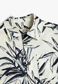 Korte mouwen overhemd met een crèmeachtige achtergrond, voorzien van een blauwe botanische print, knoopsluiting en een borstzak aan de linkerkant.