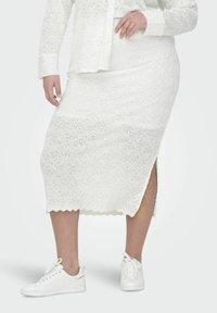 Witte kanten midi-rok met spiraalpatroon, gegolfde zoom en zijsplit, gecombineerd met witte sneakers. Heeft een semi-doorzichtige textuur.