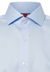 Camicia azzurra chiara con colletto aperto, caratterizzata da bottoni bianchi in plastica, texture liscia e una leggera lucentezza.