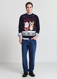 Marineblauer Weihnachtspullover mit Santa und einem Rentier, gestricktes Design mit roten und weißen Akzenten, kombiniert mit blauen Jeans und schwarzen Schuhen.