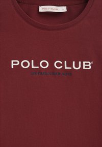 Burgundy t-shirt i mjukt material med vit broderad text "POLO CLUB" och "ETABLERAD 2012" på framsidan. Rund halsringning.