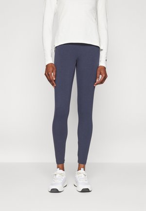 Leggings blu navy realizzati in tessuto elasticizzato, design aderente, con vita piatta, abbinati a scarpe da ginnastica bianche.