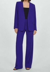 Fioletowa marynarka o kroju dopasowanym oraz pasujące szerokie spodnie wykonane z gładkiego materiału, z jedną kieszenią na piersi i dwiema kieszeniami z przodu.