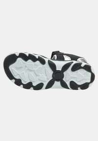 Svart atletisk sandal med en texturerad, mönstrad gummisula som har vita accenter och ett robust rem för en säker passform.