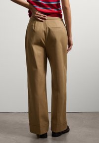 Pantalons larges beiges à texture lisse, dotés d'une poche arrière et de ourlets retroussés, associés à un haut rayé rouge.
