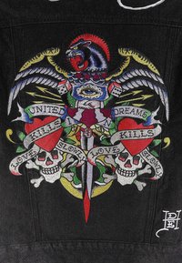 Il tessuto in denim nero presenta un colorato design ricamato con un leone, un aquila, due teschi, una spada e banner con iscrizioni di testo.