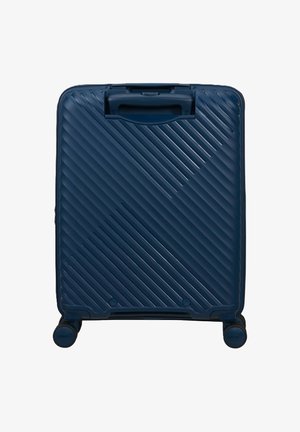 Valigia rigida blu scuro con scanalature diagonali, quattro ruote e manico superiore, in posizione verticale su sfondo bianco.