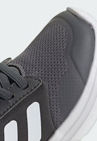 Gray athletic shoe with mesh fabric, textured overlay, and white accents. Features a lace-up design and a cushioned sole.