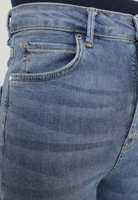 Lähikuva sinisistä farkuista vyötärö- ja taskualueesta, jossa näkyvät ompeleet ja vyölenkit.