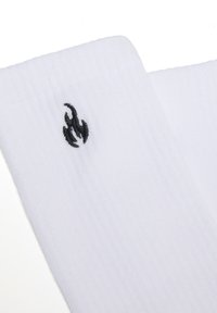 Tela blanca con canalé y un pequeño logotipo de llama bordado en negro cerca del borde superior, sobre un fondo blanco liso.