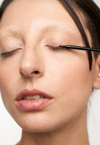 Nahaufnahme eines Gesichts, das schwarzen Eyeliner aufträgt, mit glatter Haut, neutraler Lippenfarbe und hellen, natürlichen Make-up-Tönen rund um die Augen.