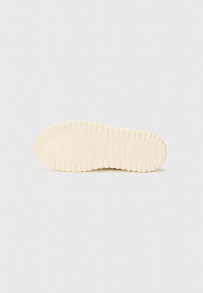 Conception de semelle de chaussure en crème clair, en caoutchouc texturé avec des nervures pour l'adhérence, bords arrondis, profil plat et branding minimal.