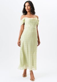 Light green midi dress with off-shoulder sleeves, featuring gold dot patterns. Made from a sheer material with a flowy silhouette and slits.