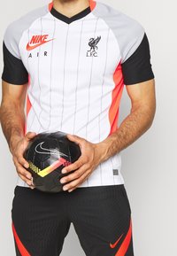 Nike-jalkapallopaita, jossa on valkoinen runko, pystysuoria harmaita raitoja, mustat hihat ja oransseja yksityiskohtia. Päällä L.F.C.-logo ja sen vieressä musta jalkapallo.