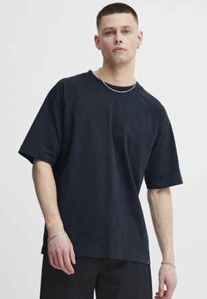 Tricou din bumbac de culoare albastru închis, cu mâneci raglan scurte și o croială lejeră. Are guler rotund și o etichetă mică la tiv.