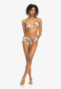 Cvečni bikini komplet z braletko, ki ima nastavljive naramnice in visokotrdne hlačke s stranskimi kravaticami v živahnih roza, zeleni in kremni vzorci.