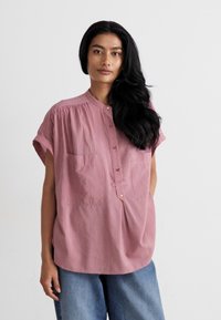 Ροζ ριγέ κοντομάνικο μπλουζάκι με γιακά, κλείσιμο με κουμπιά μπροστά και δύο τσέπες στο στήθος, σε συνδυασμό με χαλαρά μπλε τζιν παντελόνια.