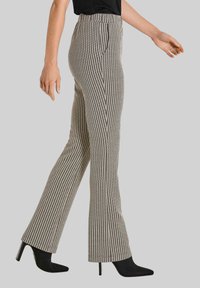 Broek met een houndstooth patroon, zwart en wit, met een uitlopende pasvorm. Hoge taille, zijzakken, gecombineerd met zwarte leren enkellaarsjes met hakken.