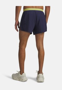 Navy blue athletic shorts with a yellow elastic waistband, featuring side slits and a lightweight texture, paired with white running shoes.