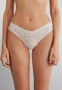 Kanten slip met een crèmekleur, gegolfde randen, een gedetailleerd bloemenpatroon en een zachte tailleband, ontworpen voor comfort en esthetiek.