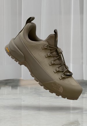Beige tursko for trekking med en teksturert overdel, snøresystem og Vibram såle. Har The North Face-logoen og en forsterket tåhette.