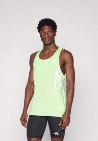 Groen atletisch tanktop met witte strepen, gemaakt van ademend materiaal. G gedragen met zwarte shorts met een klein logo op de dij.