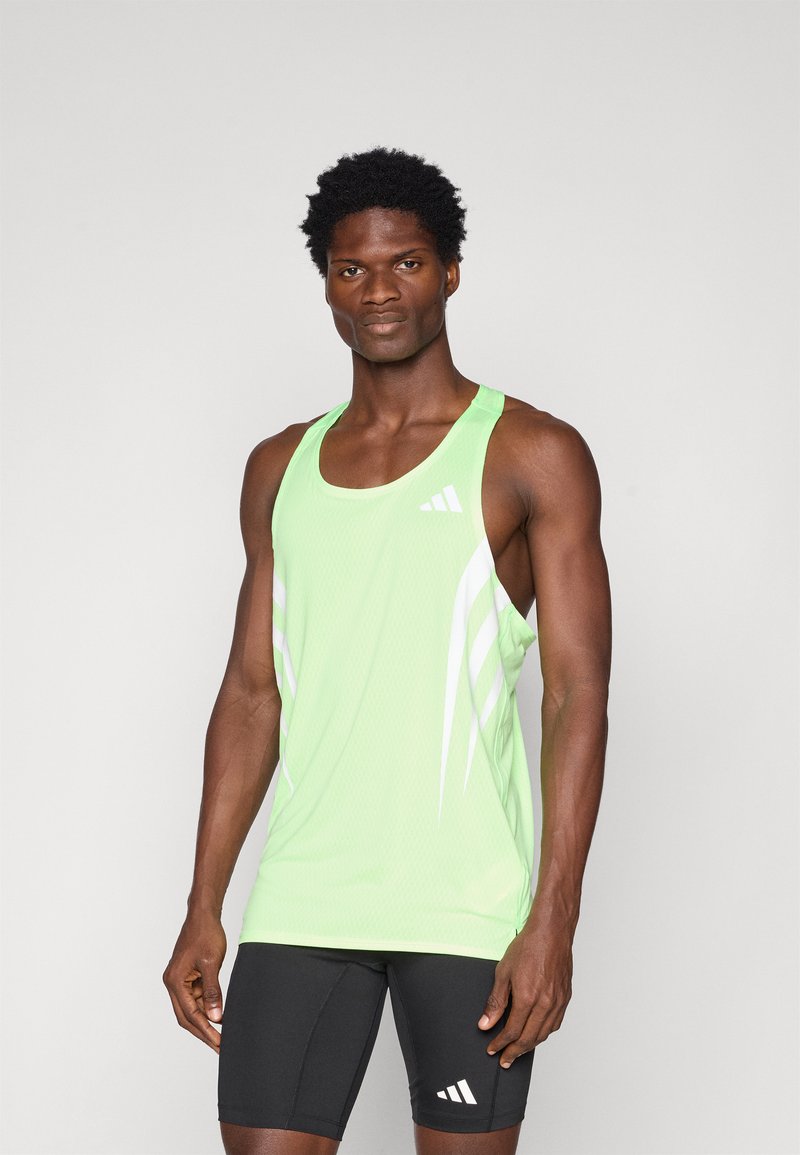 Grünes sportliches Tanktop mit weißen Streifen, aus atmungsaktivem Material hergestellt. Getragen mit schwarzen Shorts, die ein kleines Logo am Oberschenkel haben.