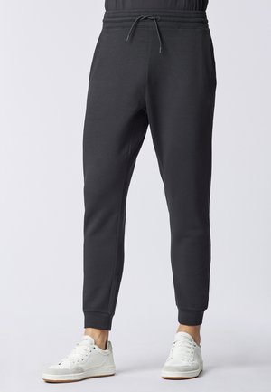 Pantaloni della tuta grigio scuro in tessuto morbido, con coulisse in vita, gambe affusolate e tasche laterali, abbinati a scarpe da ginnastica bianche.