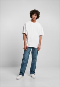 T-shirt bianca oversize con maniche corte, abbinata a jeans dritti azzurri chiari e sneakers bianche. Tessuto semplice, senza motivi visibili.