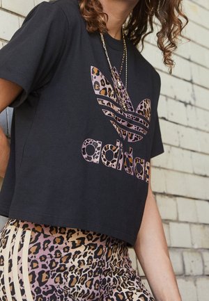 Persona que lleva una camiseta corta negra de Adidas con logo de estampado de leopardo y leggins a juego con estampado de leopardo y rayas claras en los laterales.