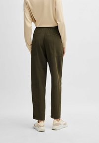 Olijfgroene tapered broeken met elastische tailleband, zijzakken en patchwork stiksels. Gepaard met een beige langwerpig shirt en lichte sneakers.