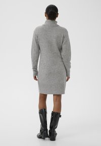 Robe en tricot gris avec un col montant, des manches longues et un ourlet côtelé. Portée avec des bottes noires arrivant au genou, ornées de boucles et à talon épais.