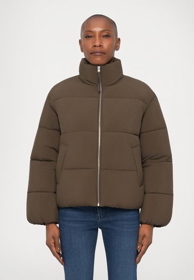 Veste matelassée marron avec un col haut, dotée d'une fermeture éclair à l'avant, de coutures horizontales et de poignets élastiques. Portée sur un jean en denim.