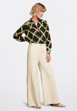 Blouse noire avec un motif géométrique coloré, associée à un pantalon large crème taille haute. Comprend une fermeture à boutons et des poches latérales.