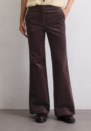 Braune Corduroy-Hosen mit Schlag, glatter Textur, hohem Bund und seitlichen Taschen, kombiniert mit dunklem Schuhwerk auf einem neutralen Hintergrund.
